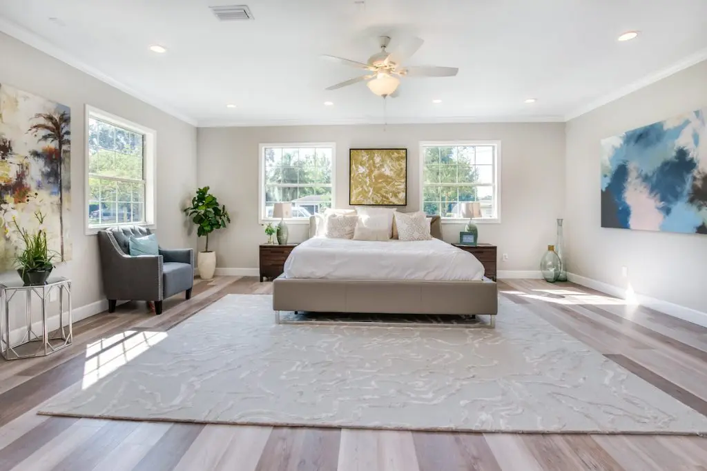 Spacious master bedroom with large rug, bed, armchair, nightstands, and artwork staged by MHM Professional Staging for Zombie House Flipping season three episode one.
