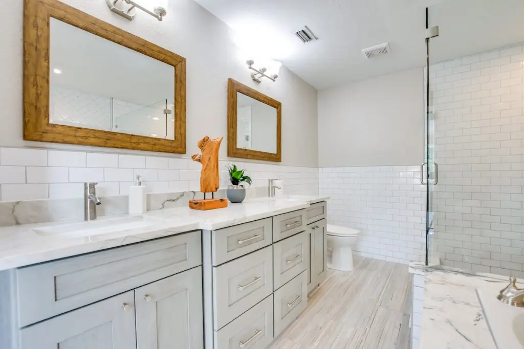 Master bathroom counter top with double sinks, wooden mirrors, wooden decor, and a plant staged by MHM Professional Staging for Zombie House Flipping season three episode one.