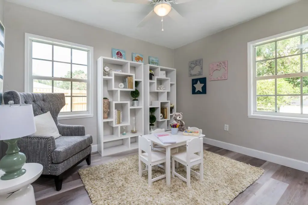 Another view of the kids playroom with rug, styled shelves, a kids table, and gray armchair.