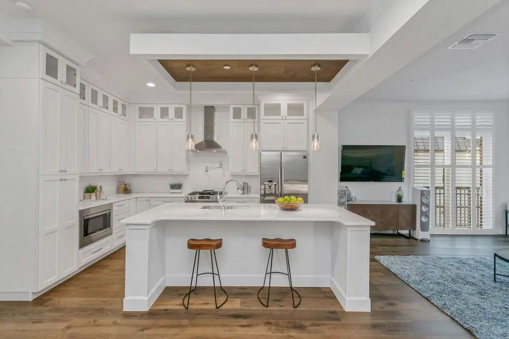 An all white kitchen with brown barstools and wooden accent overhead.